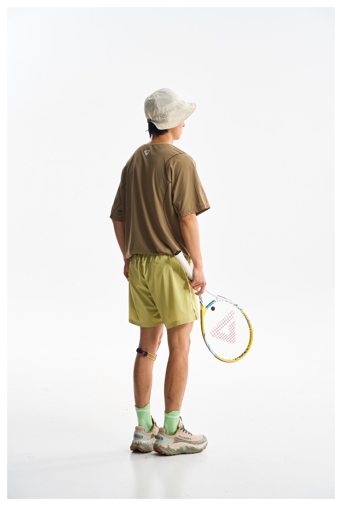 Back view of a model wearing a brown short-sleeve shirt and light yellow-green shorts.