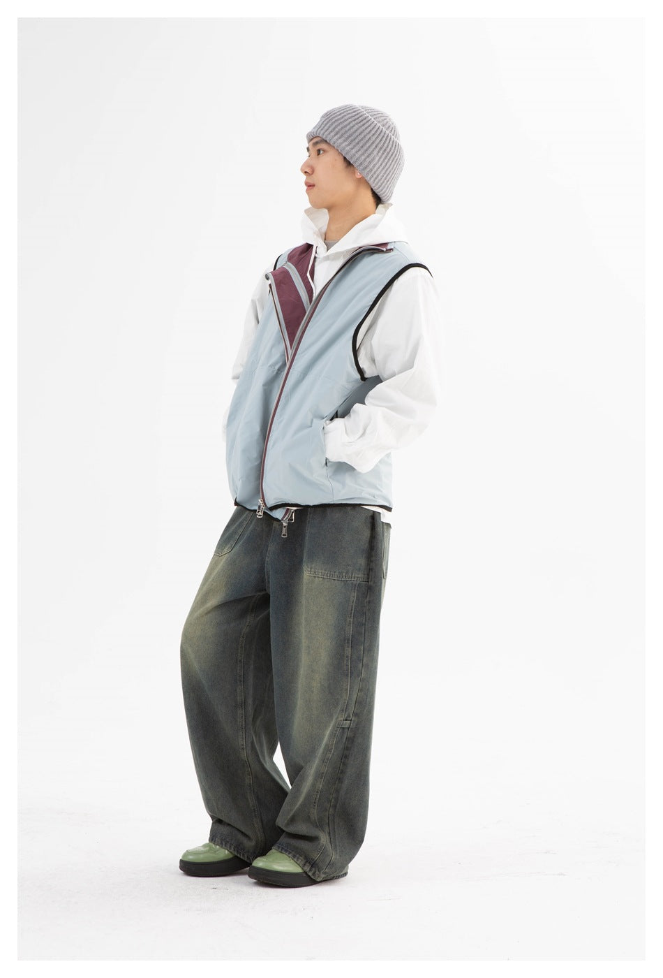 Side view of a model wearing a pale blue sleeveless zip vest with burgundy lining over white layers and dark jeans.