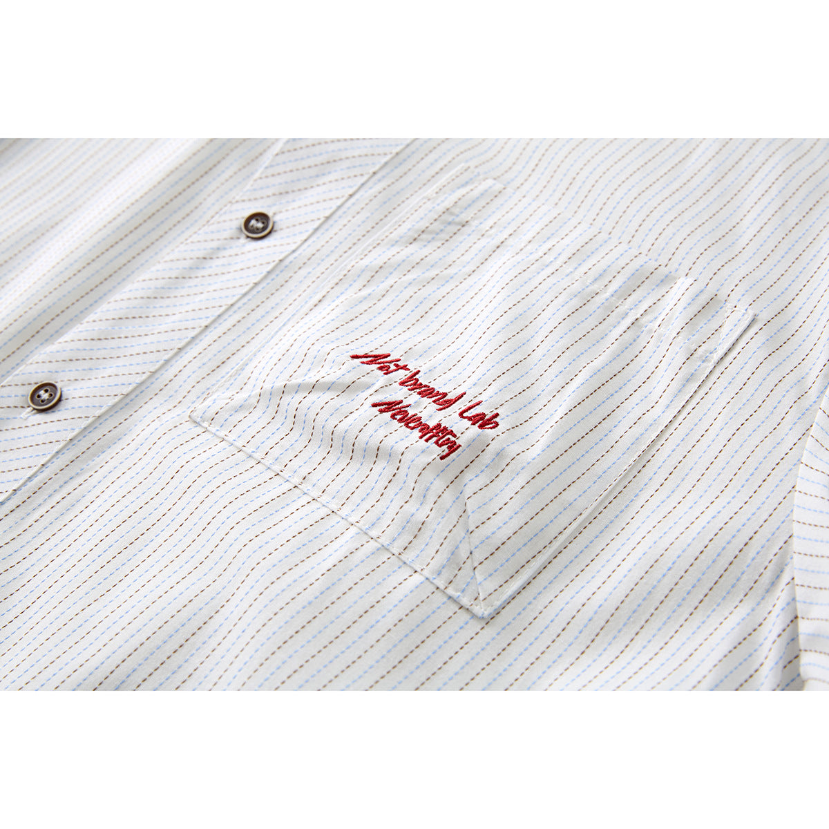 Close-up of a striped white shirt pocket with red embroidered lettering and dark buttons.