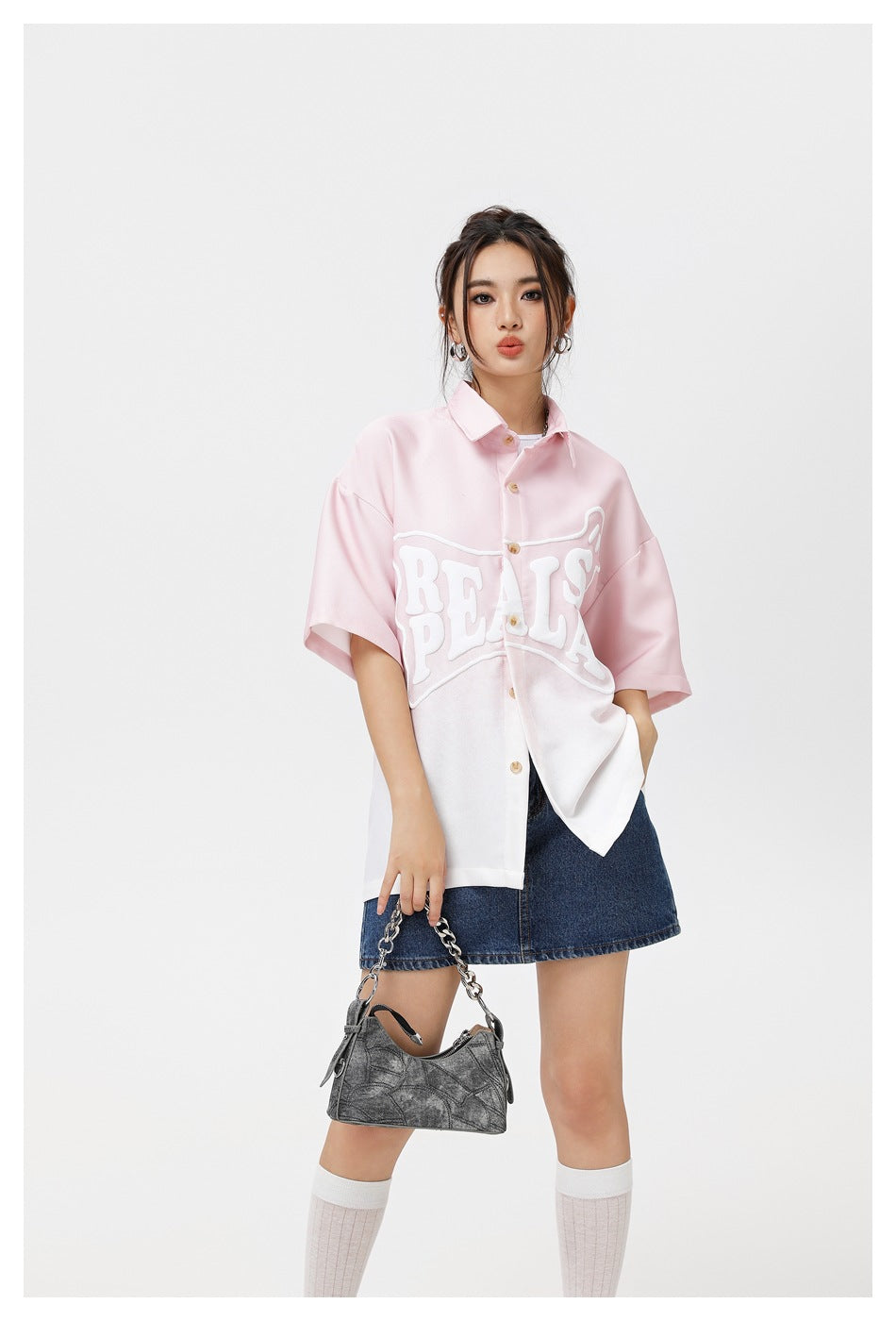 Closer view of a model wearing an oversized pink-to-white short-sleeve shirt with raised white lettering and a denim skirt.
