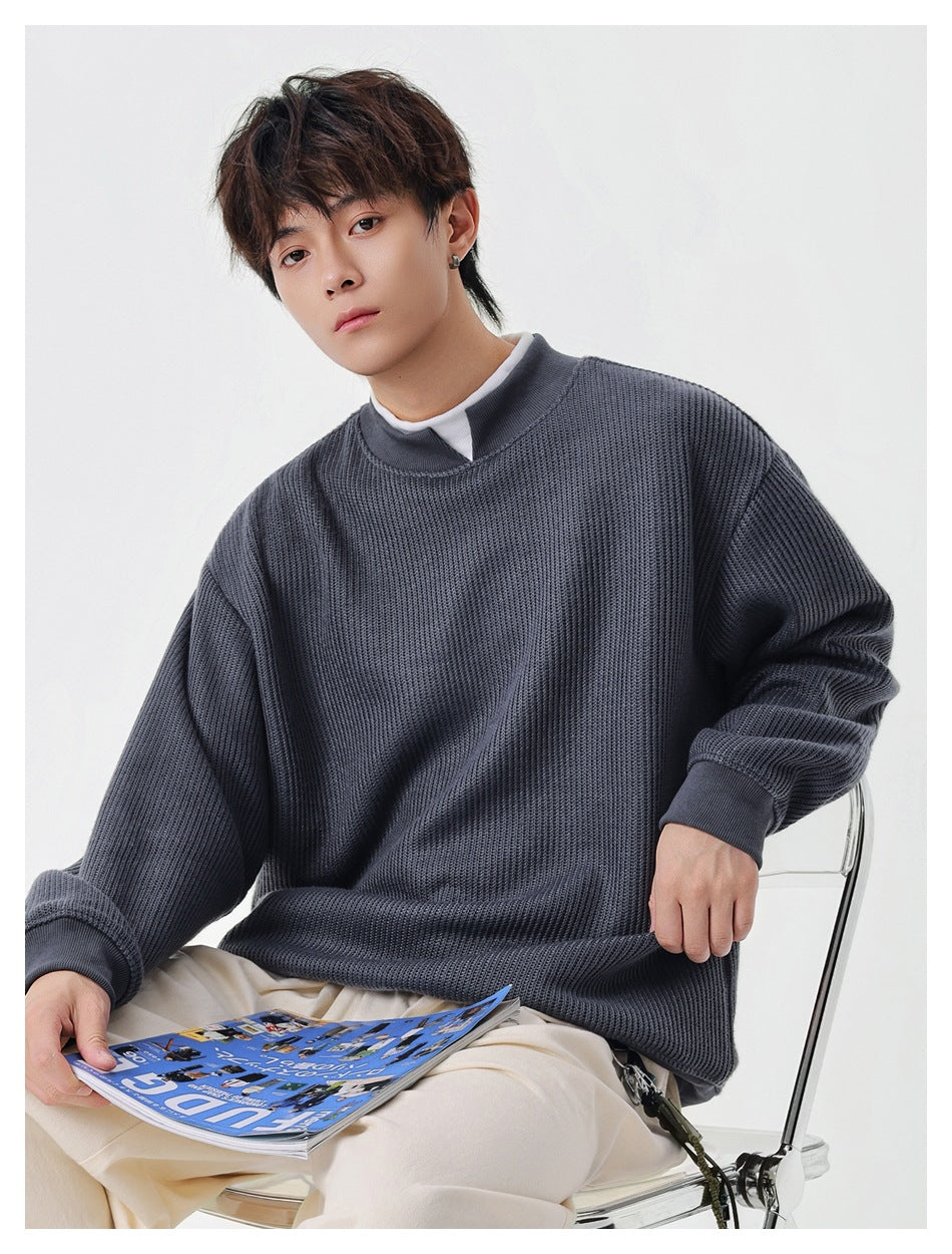 Seated model wearing a slate gray-blue ribbed sweatshirt with a stand collar and ribbed cuffs.