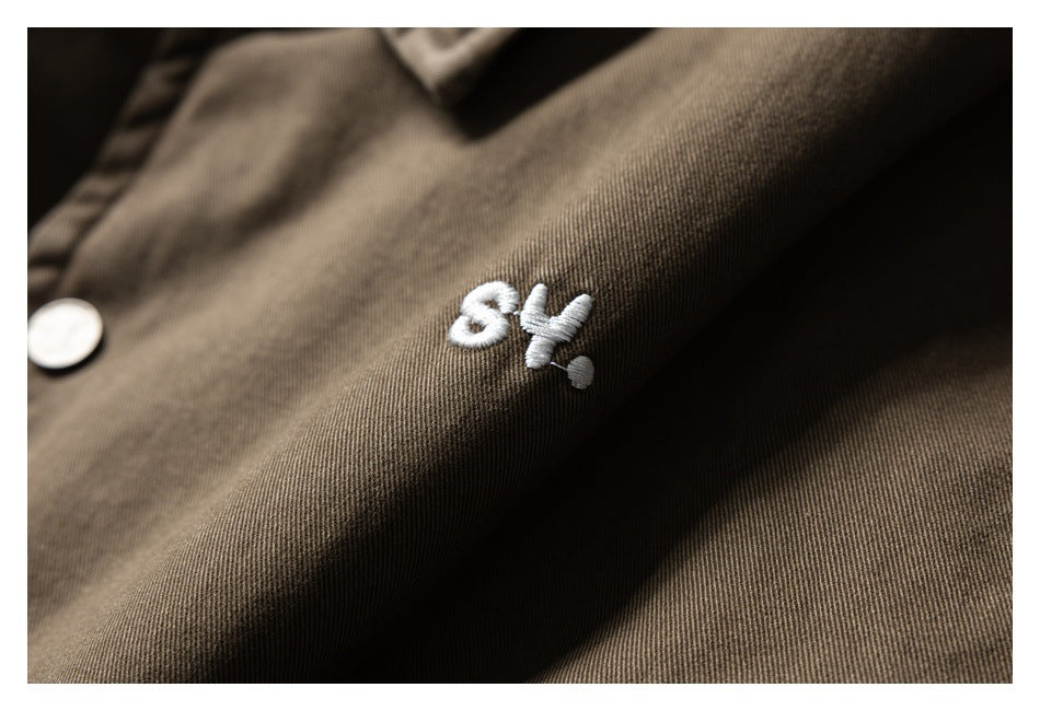 Close-up of a small white embroidered motif on the brown jacket beside a silver snap.