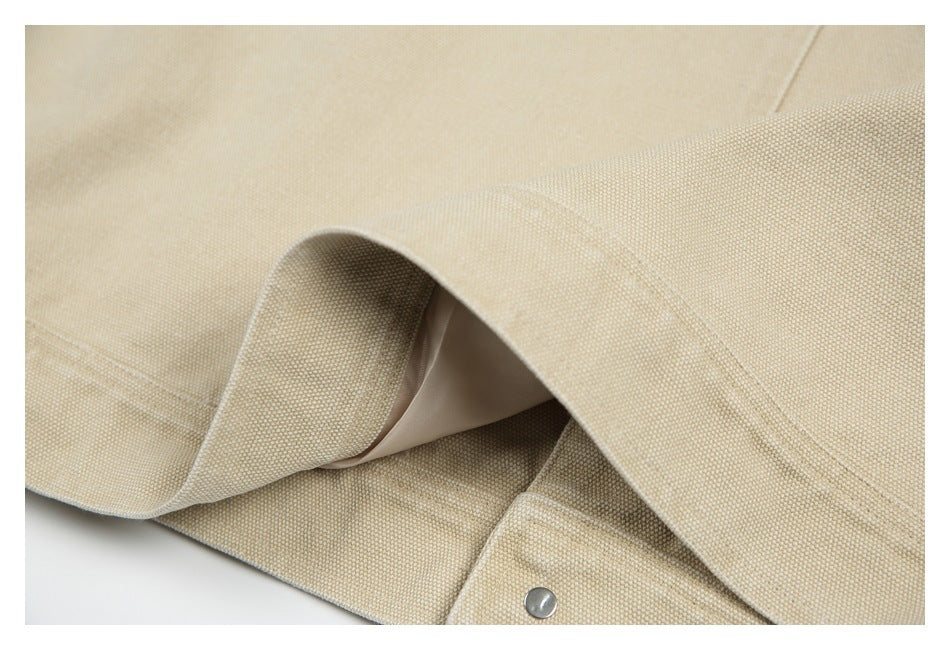 Close-up of a beige woven jacket edge, folded seam, pale lining and metal snap.