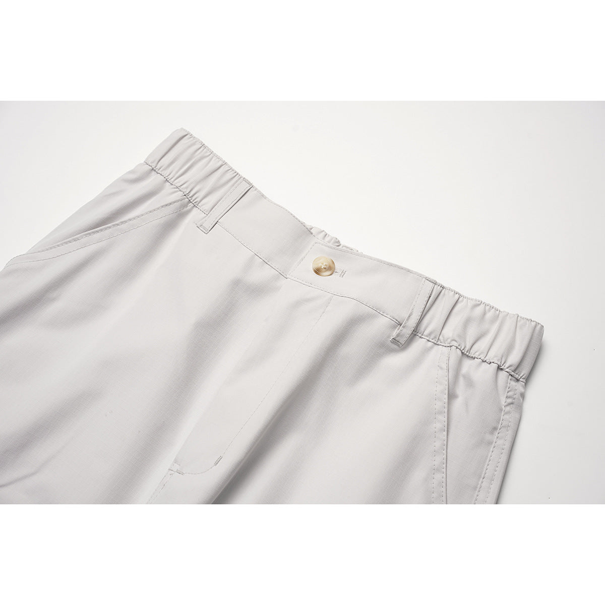 Close-up of light gray pants showing the button closure, belt loops, and elasticated waistband sides.