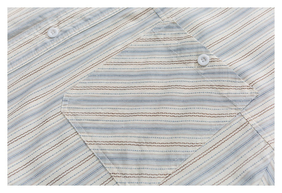 Close-up of a white button and pocket on cream fabric with fine blue and brown stripes.