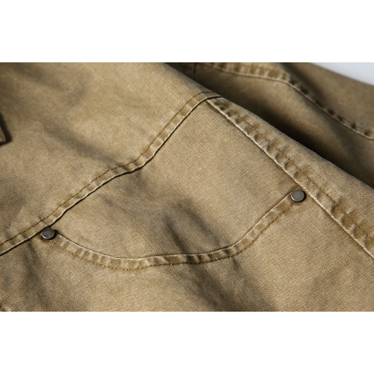 Close-up of a tan-brown jacket pocket with curved stitching and metal rivets.