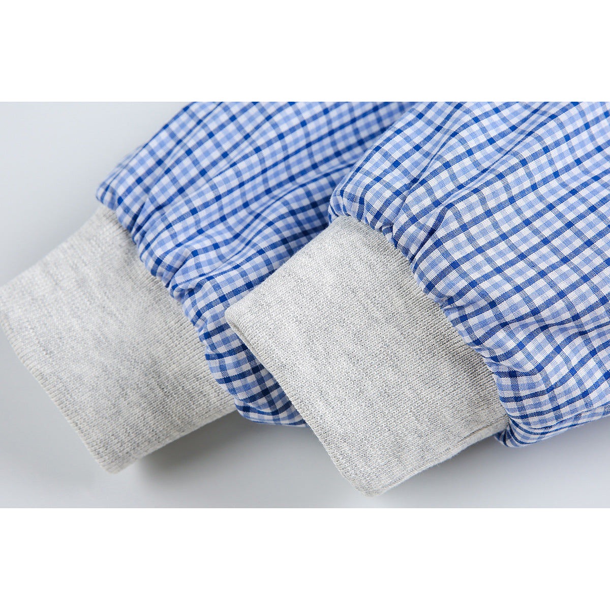 Close-up of gray ribbed cuffs beside blue-and-white plaid hoodie sleeves.