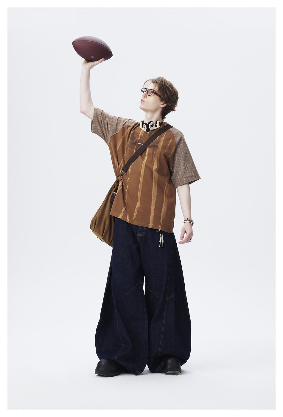 Model raising a football while wearing a brown streaked raglan T-shirt with striped sleeves and wide dark jeans