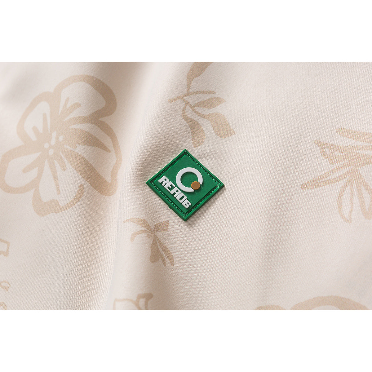 Close-up of a green diamond-shaped patch on beige floral fabric.