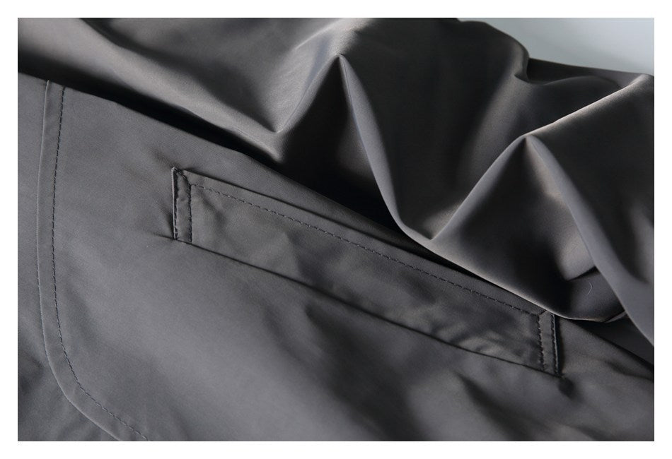 Close-up of a charcoal-gray jacket with a stitched flap pocket and curved seam.
