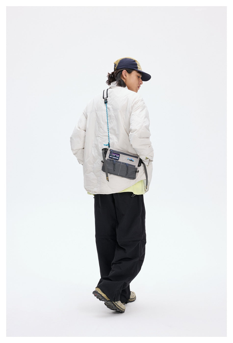 Back view of a model in a light gray quilted jacket with a crossbody bag and black pants