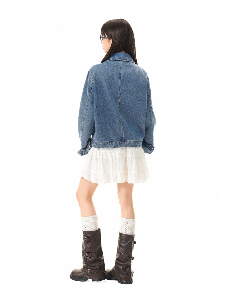 Back view of a model wearing a blue denim jacket with a center back seam and a white skirt.