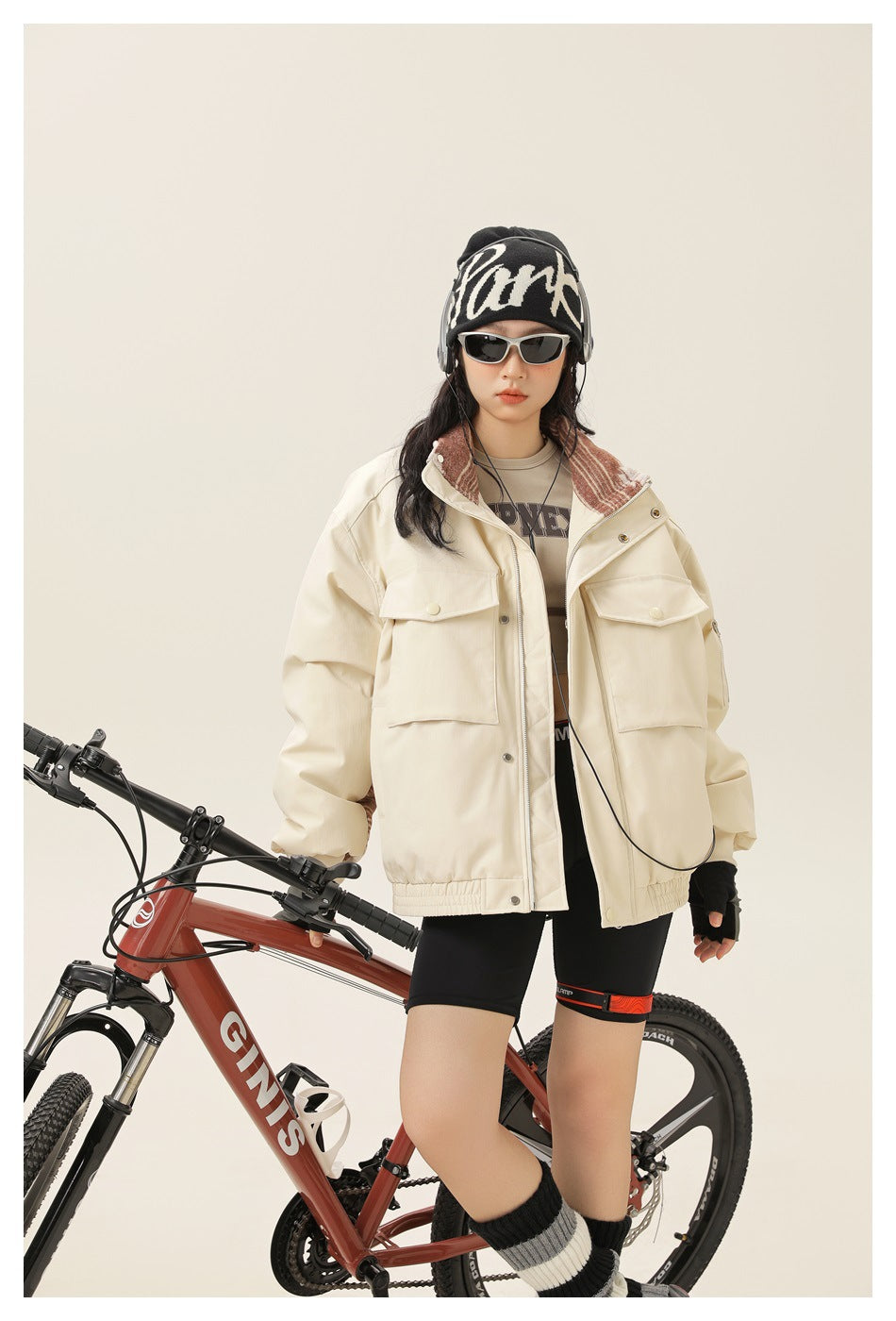 Model wearing an off-white zip jacket with large flap chest pockets, standing beside a red mountain bike