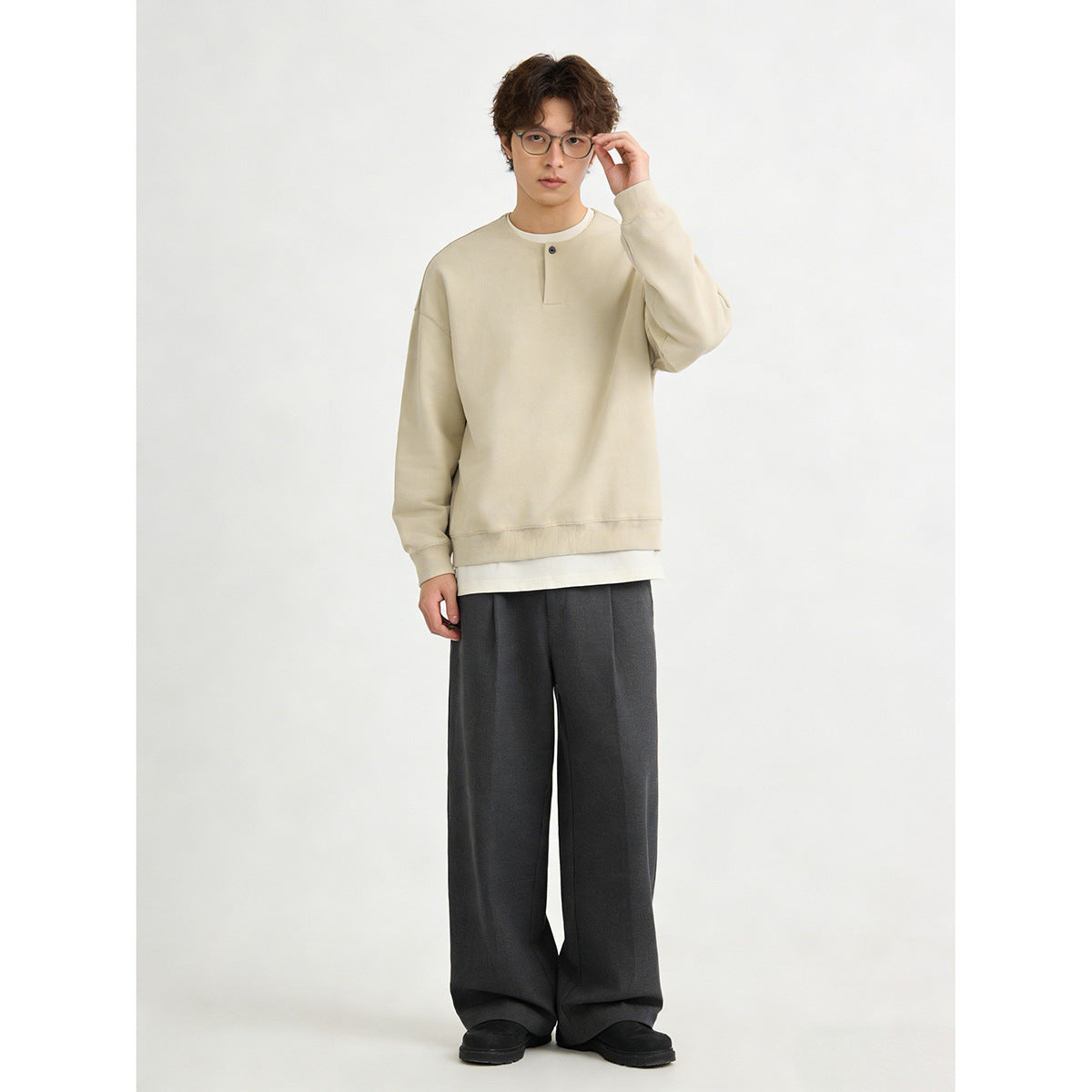 Full-length model wearing a light beige oversized button-placket sweatshirt with dark wide-leg trousers.