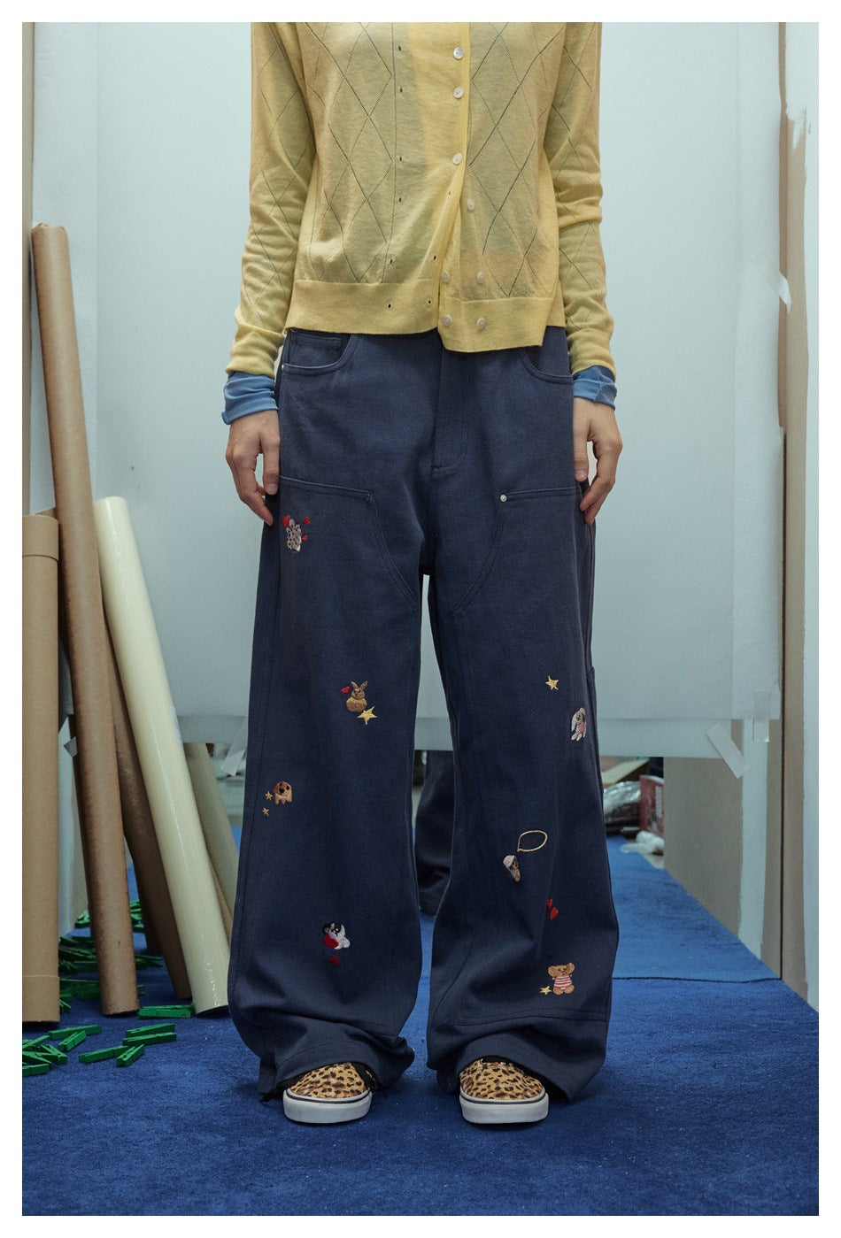 Person wearing navy embroidered wide-leg pants with a yellow cardigan and leopard print sneakers, cropped at the waist