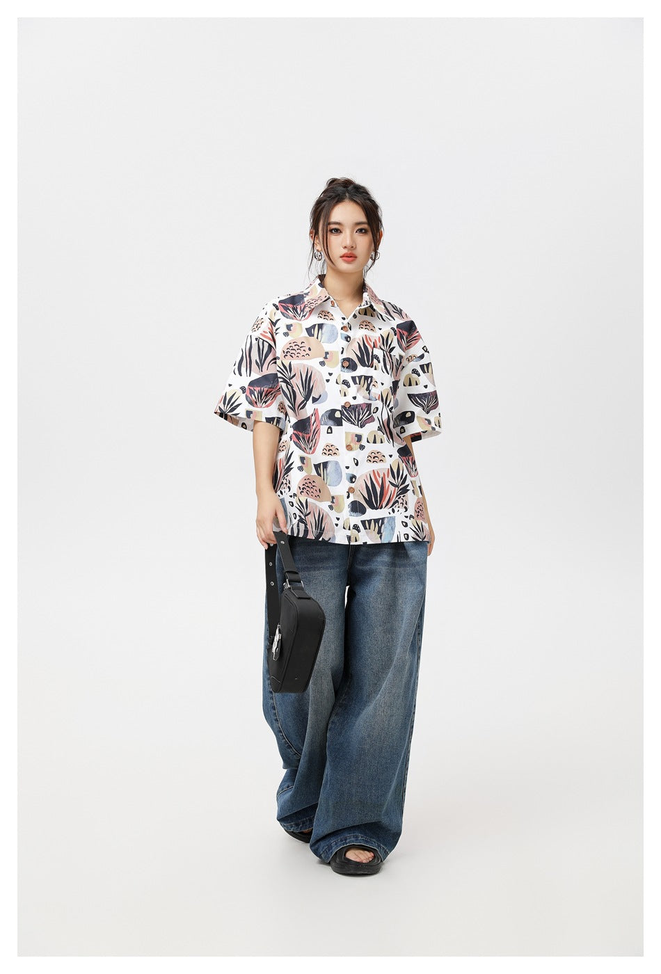 Model wearing buttoned botanical-print short-sleeve shirt with wide-leg jeans, carrying a black shoulder bag
