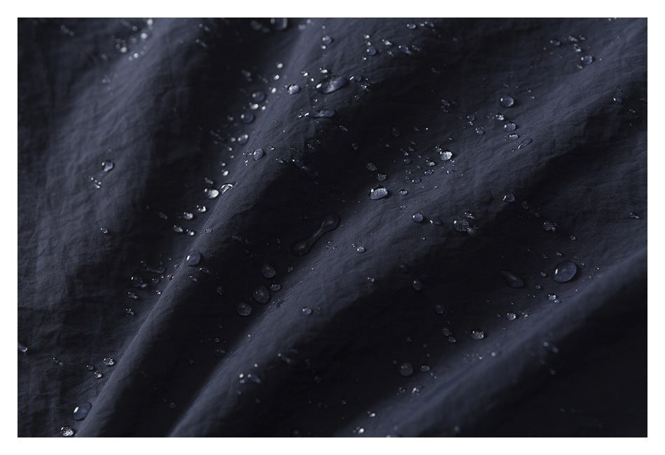 Water droplets bead on the surface of dark navy garment fabric.
