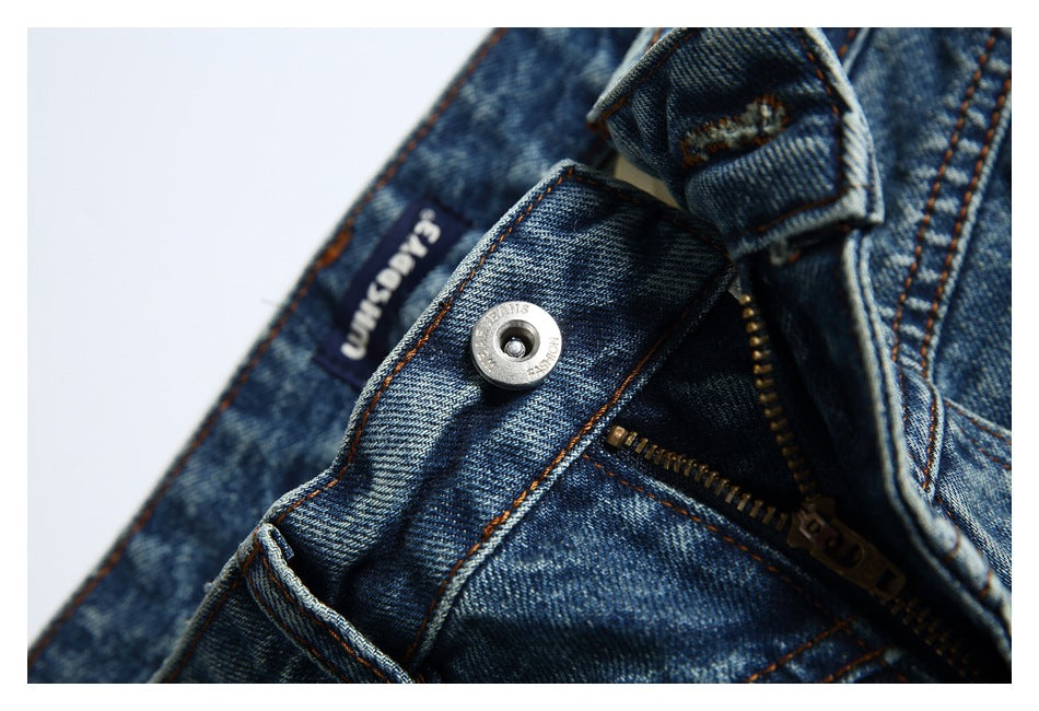 Close-up of the jeans' waistband, metal button, belt loop, and partially open zipper.