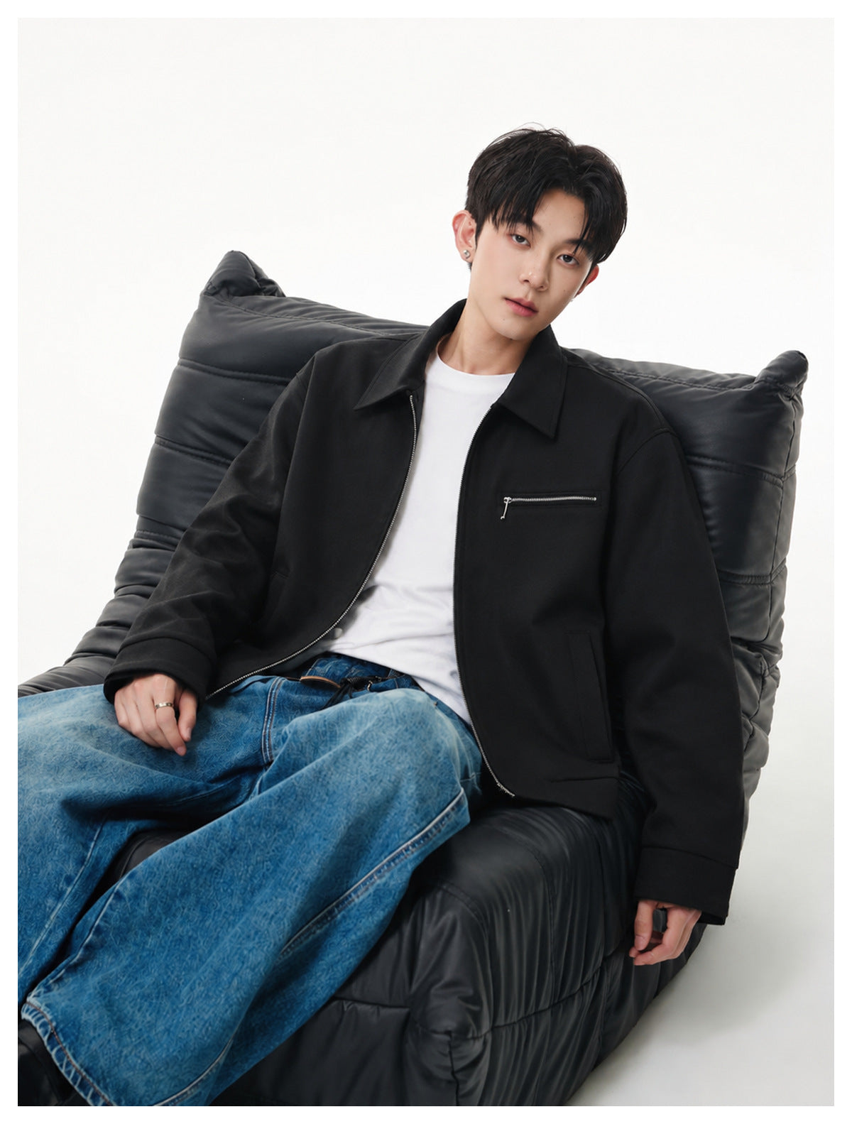 Seated model wearing an open black collared jacket with a chest zip pocket over a white T-shirt.