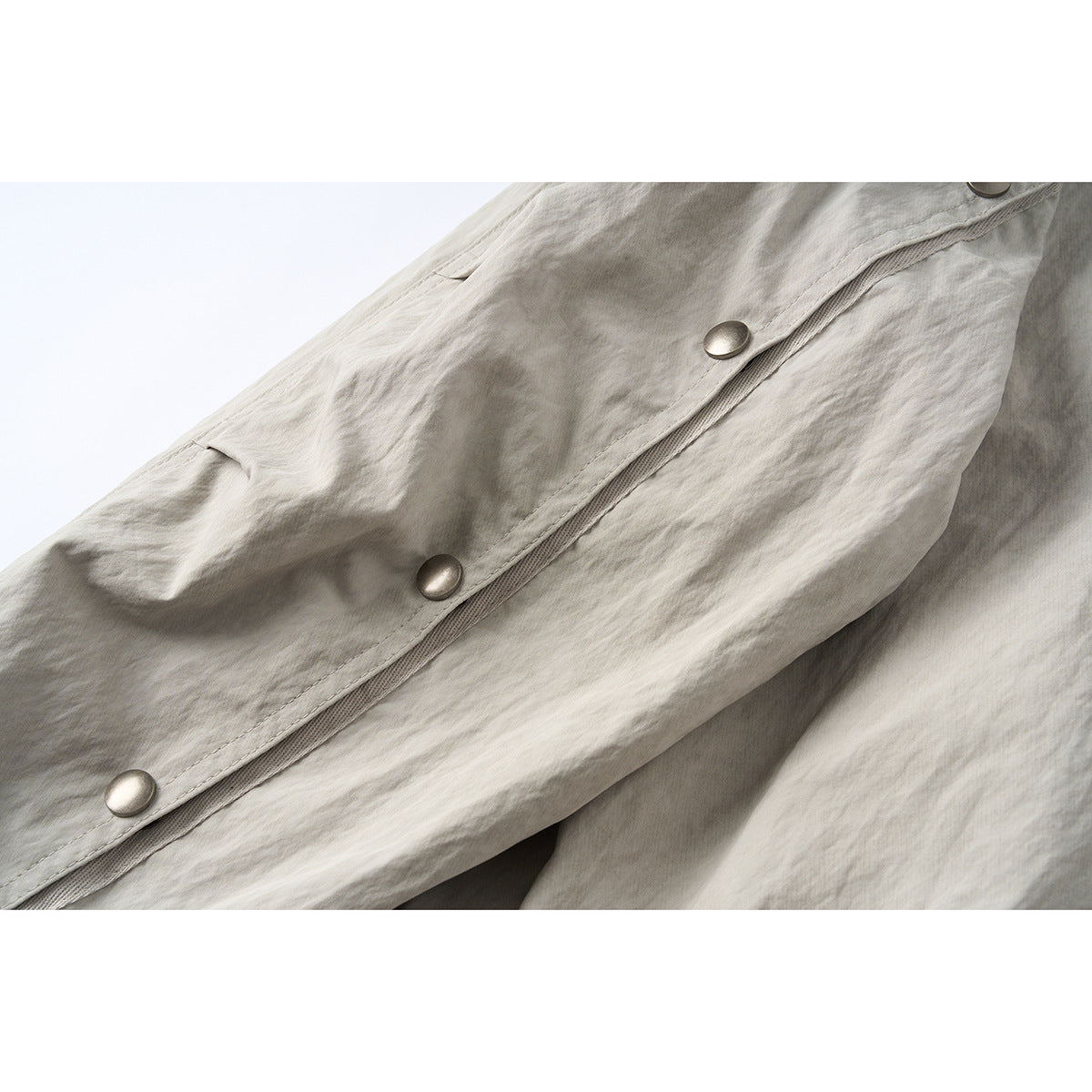 Close-up of the light gray-beige jacket's diagonal snap-button placket with several metal snaps.