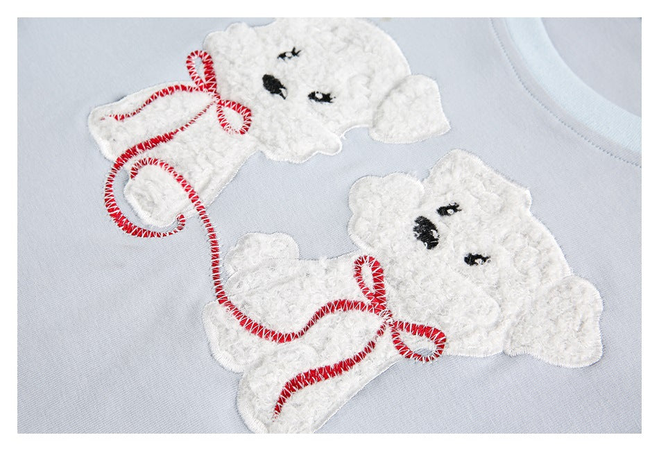 Close-up of two white teddy bear appliqués with red stitched accents on pale blue fabric.