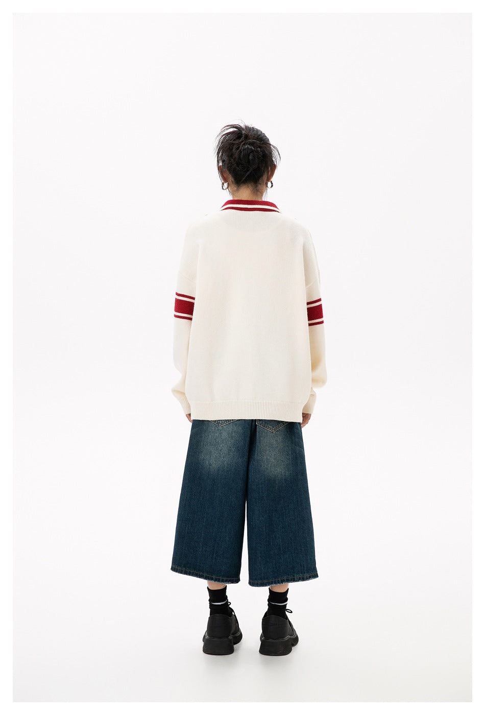 Back view of model wearing the beige knit pullover with red striped sleeves and collar, with denim shorts