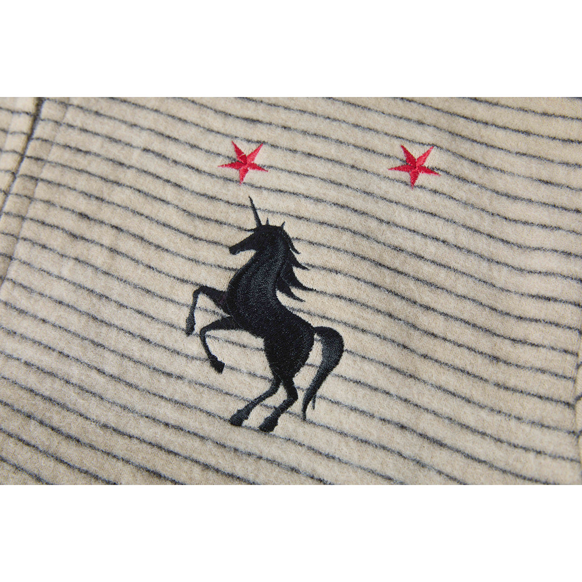 Close-up of a black rearing horse and two red stars embroidered on beige, gray-striped fabric.