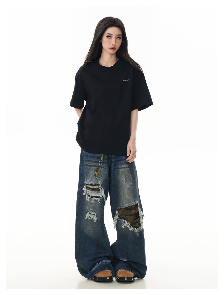 Full-length model wearing an oversized black short-sleeve T-shirt with small chest text and distressed wide-leg jeans.