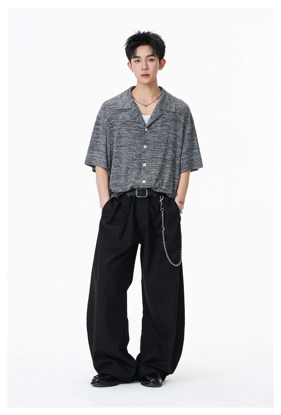 Full-length view of a model wearing a dark gray marled short-sleeve button-up shirt and black wide-leg pinstripe trousers.