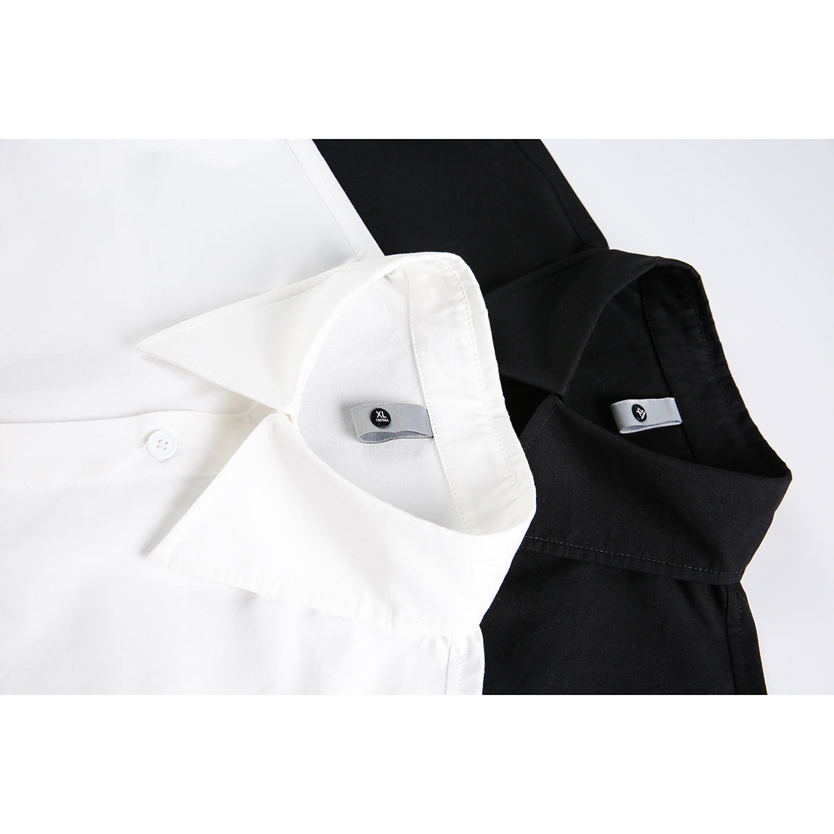 Close-up of white and black button-up shirts showing their pointed collars and small inner labels.
