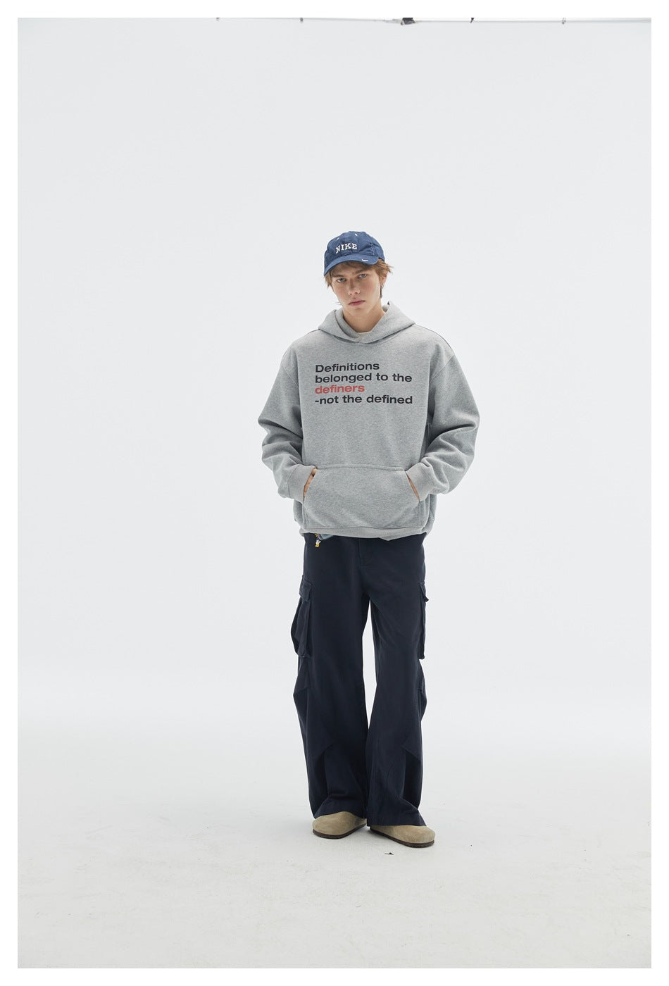 Full-length front view of a model wearing a gray slogan hoodie with kangaroo pocket and loose navy cargo pants.
