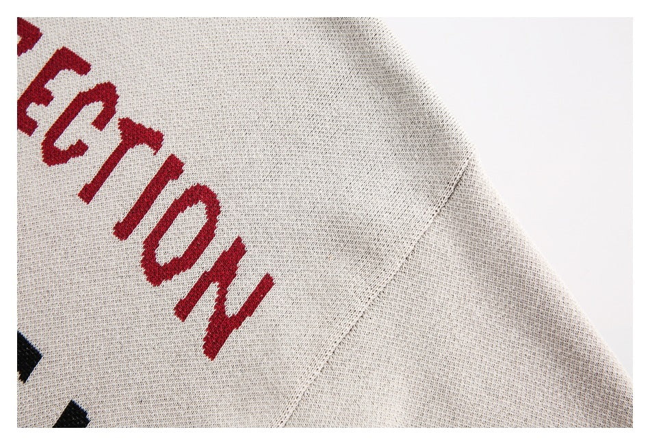 Close-up of the cream sweater's speckled knit shoulder and sleeve, beside cropped red lettering.