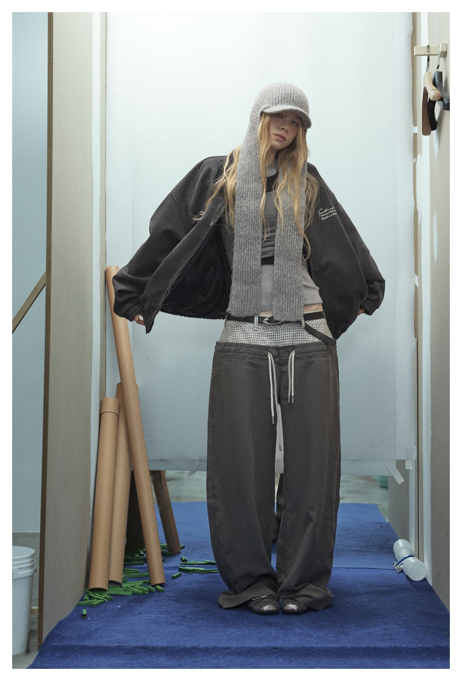 Front view of a model in an oversized charcoal zip jacket with a gray knit scarf and loose dark trousers.