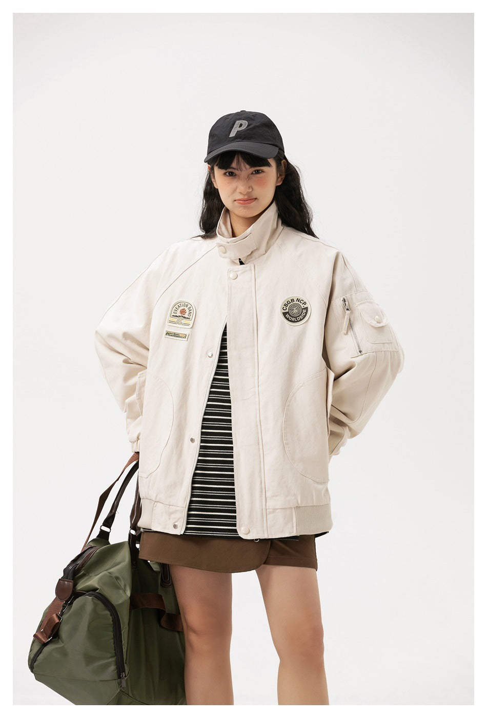Model wears an ivory jacket with a stand collar, snap front, patches, and a zippered sleeve pocket.