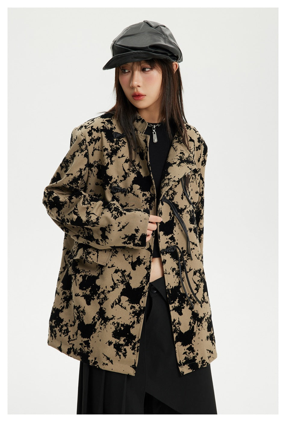 Close view of a model wearing a tan jacket with a bold black abstract pattern and black toggle closures.