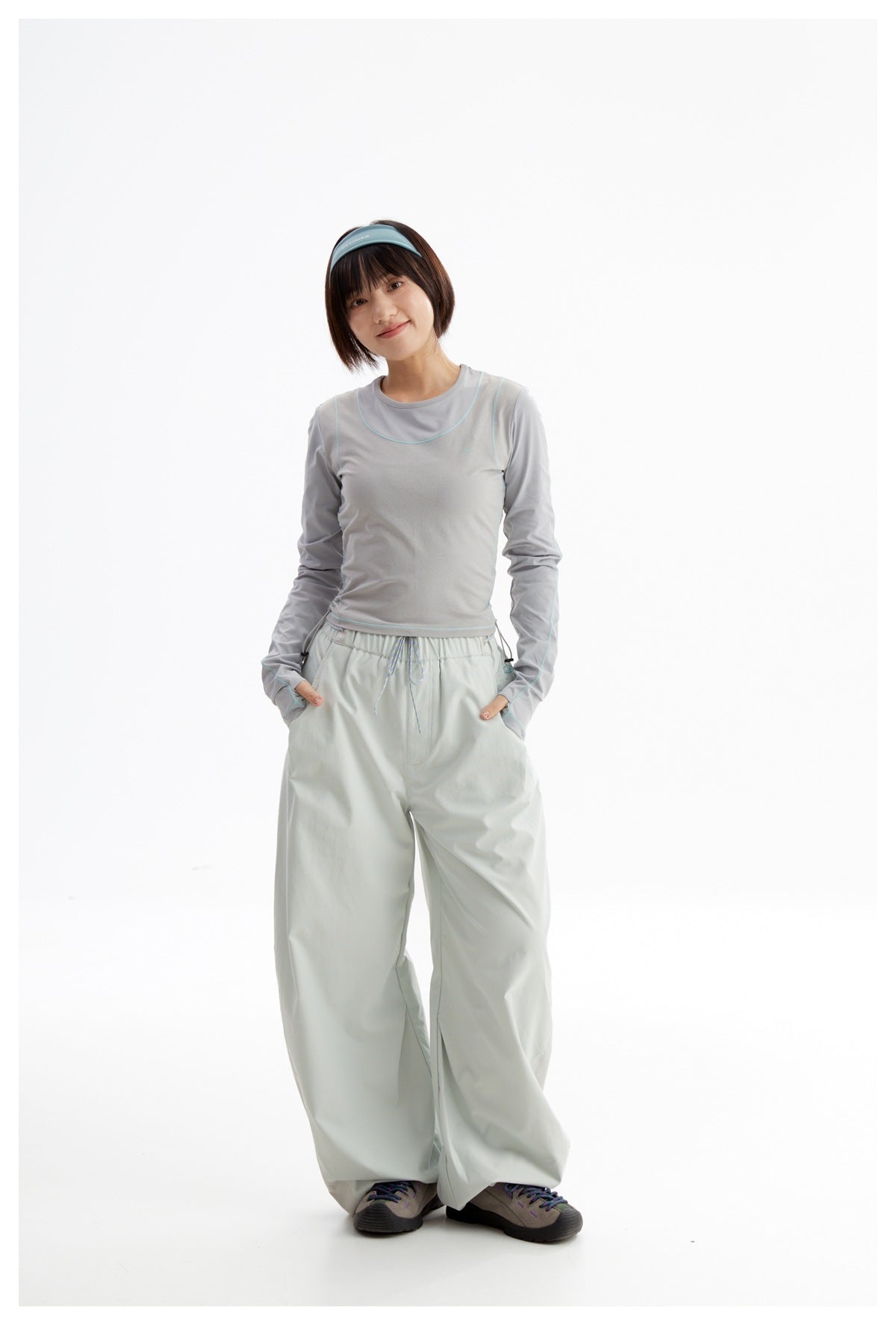 Front view of a model wearing a light gray long-sleeve top with teal piping and pale mint wide-leg pants.