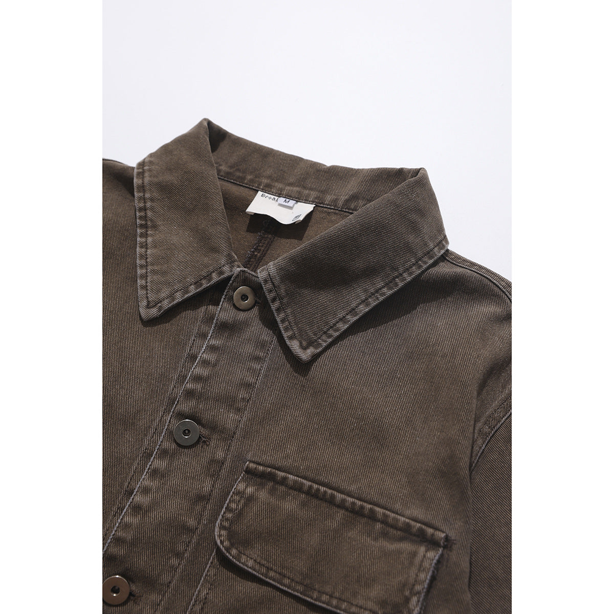 Close-up of a brown button-front shirt showing its pointed collar, chest pocket, and dark buttons.