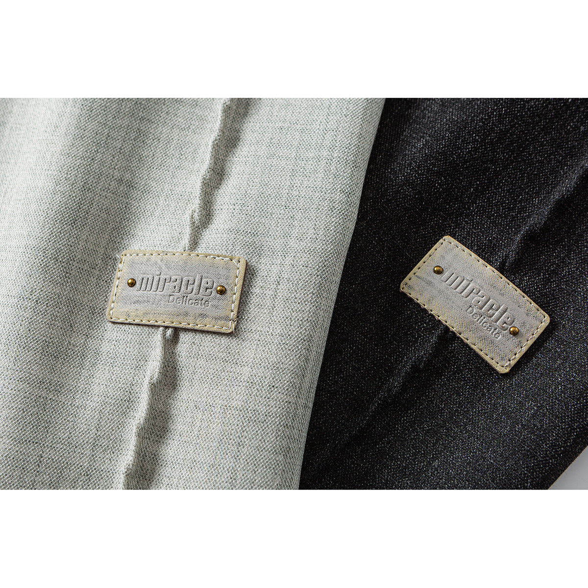 Close-up of light gray and black shirt fabric with small stitched brand patches.