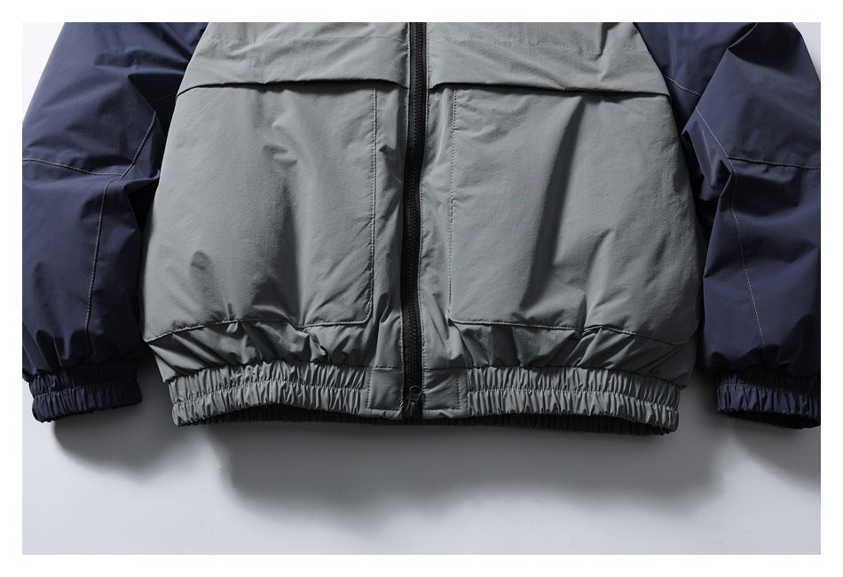 Lower front detail of the jacket, showing large gray panels, a center zipper, elastic hem, and navy sleeves.