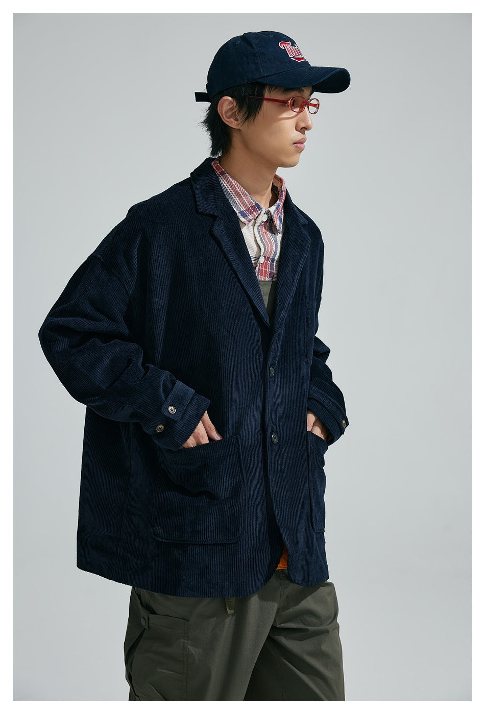 Model wearing a dark navy ribbed blazer with notch lapels, large patch pockets and buttoned cuffs over a plaid shirt.