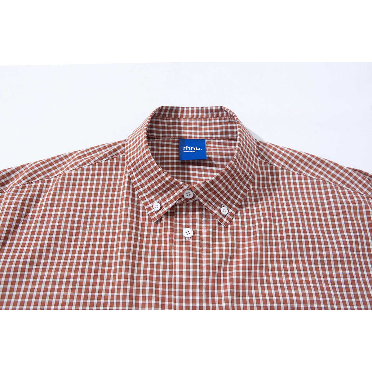 Close-up of a rust and white gingham shirt showing its button-down collar, white buttons, and blue neck label.