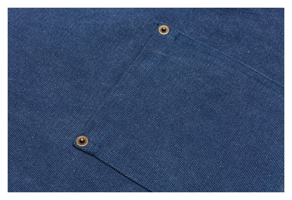 Close-up of blue woven fabric with diagonal pocket seams and two brass-tone snap fasteners.