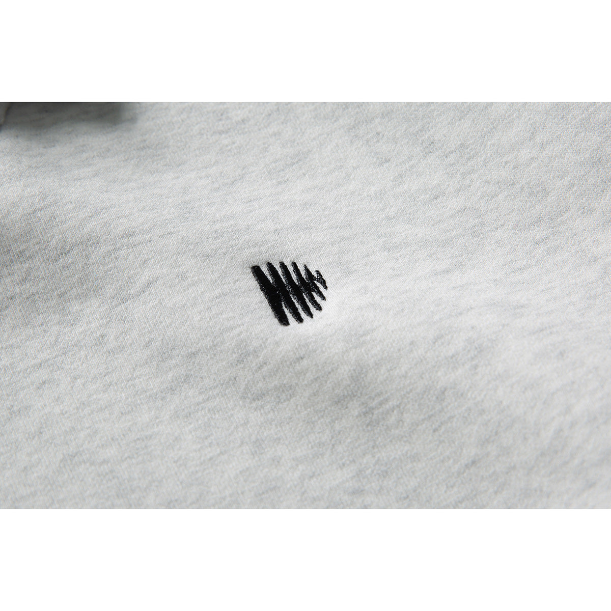 Close-up of a small black embroidered mark on light gray sweatshirt fabric.