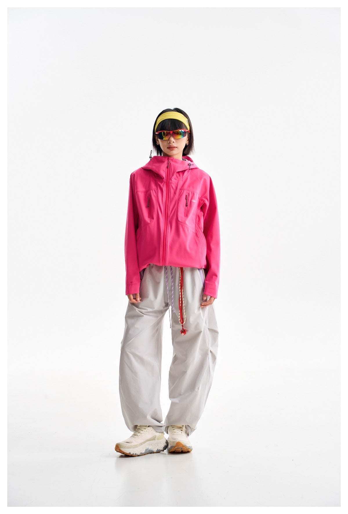 Front view of a model in a zipped bright pink hooded jacket with two chest pockets and loose light gray trousers.