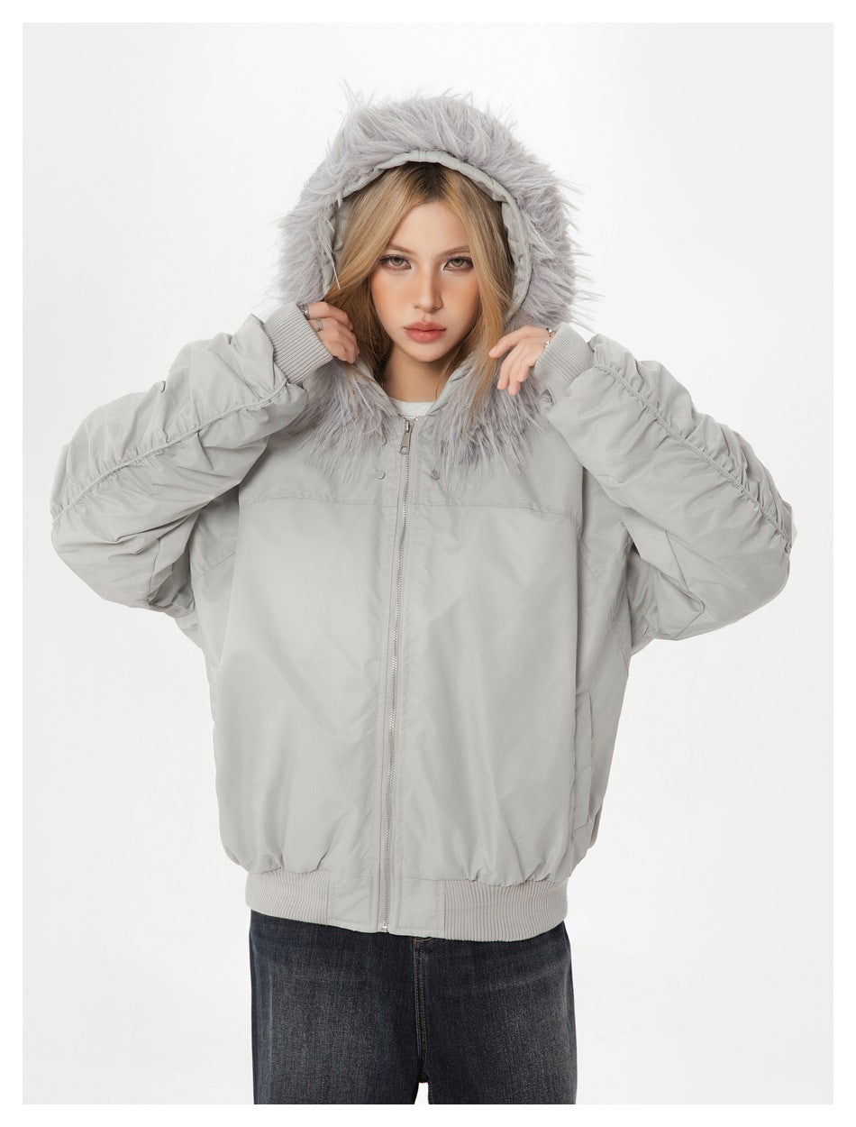 Model holding the fur-trimmed hood of a light gray zip-up jacket with gathered sleeves.