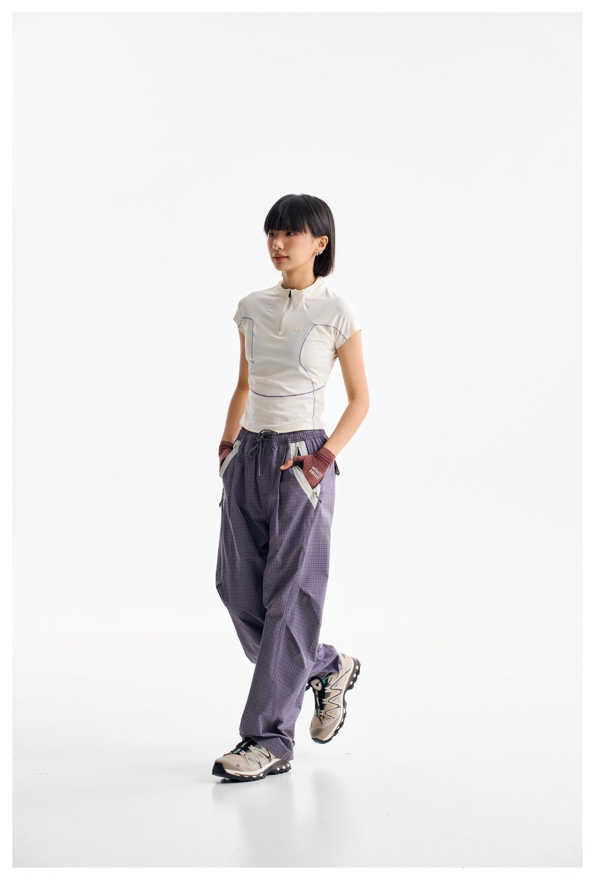 Model in a white short-sleeve quarter-zip top and loose purple plaid trousers, shown at a slight angle.