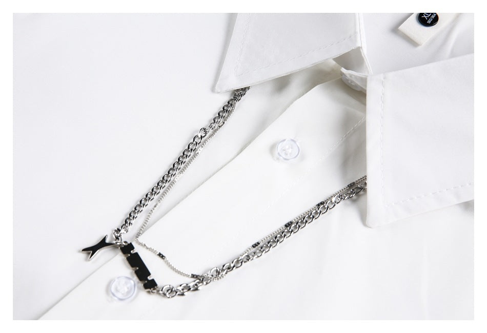 Close-up of a white shirt collar and buttons with silver chains and a black star charm.