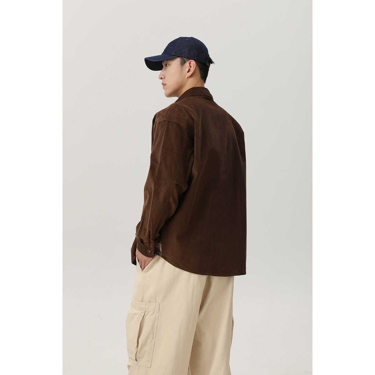Rear three-quarter view of a model wearing a brown shirt and loose cream cargo pants with a side pocket.
