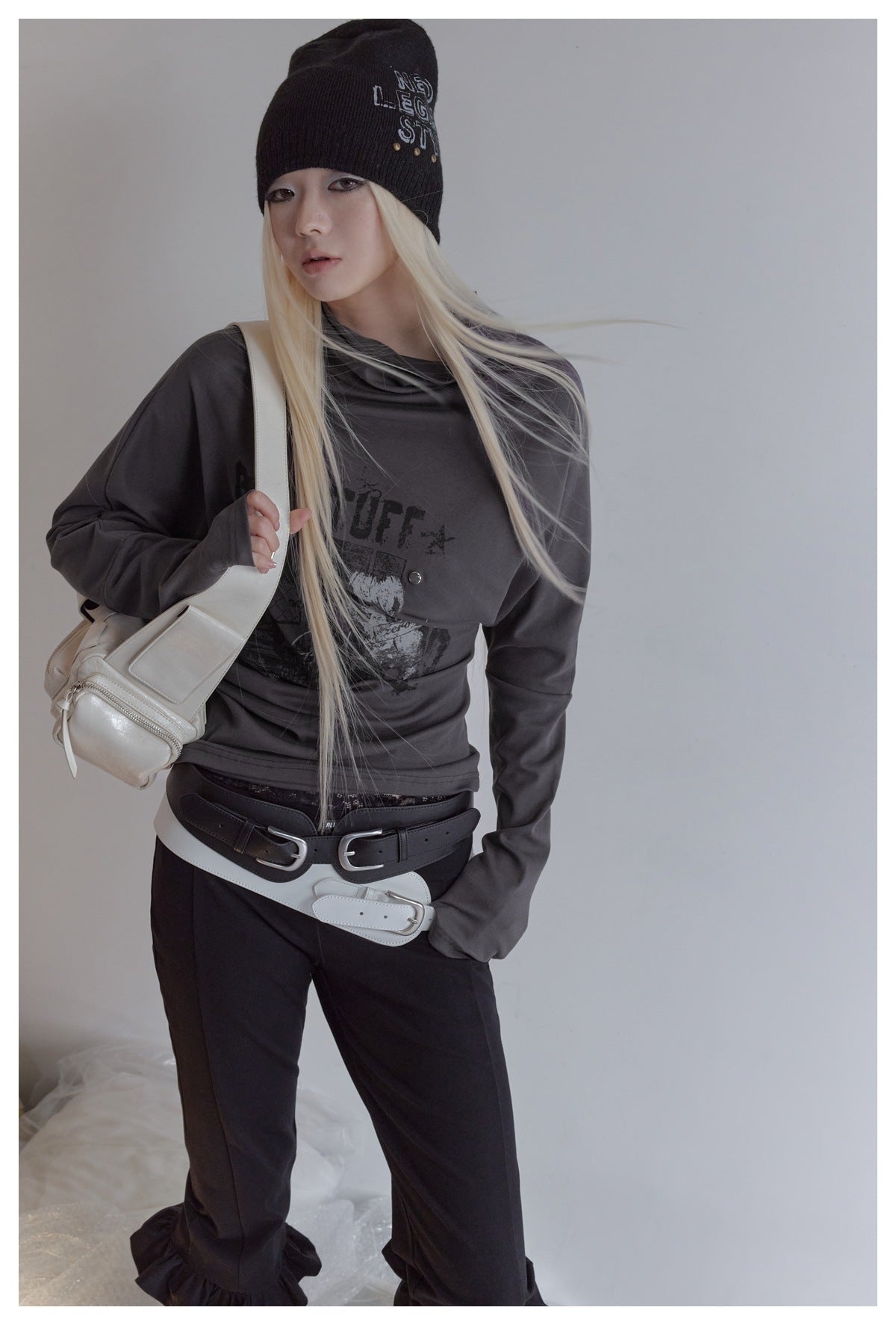 Model wearing a charcoal long-sleeve draped-neck graphic top with black trousers and layered black and white belts.