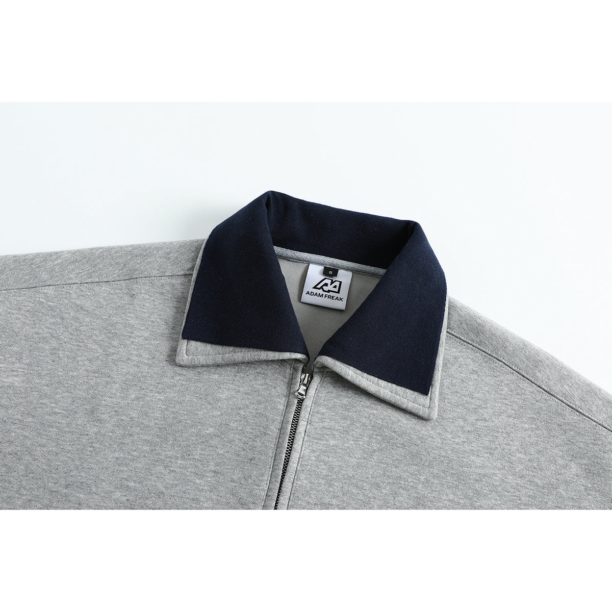 Close-up of a gray pullover's navy collar and short front zipper, with a small neck label.